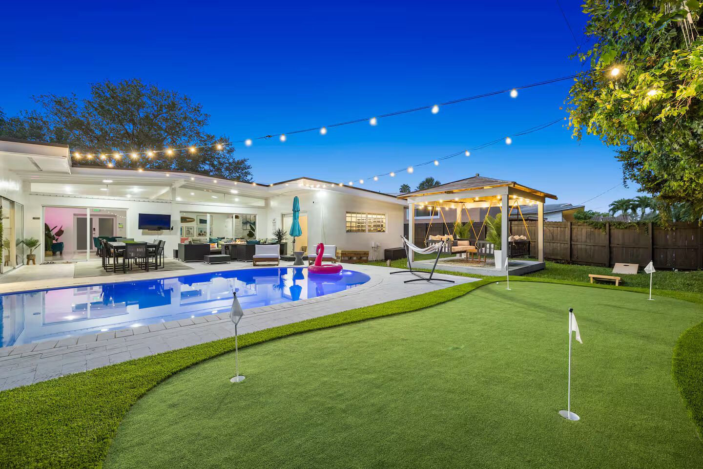 Backyard pool area with putting green and lit gazebo under string lights at twilight