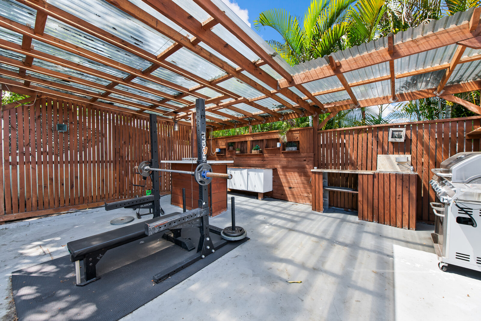 Outdoor gym area under wooden pergola with squat rack and grill