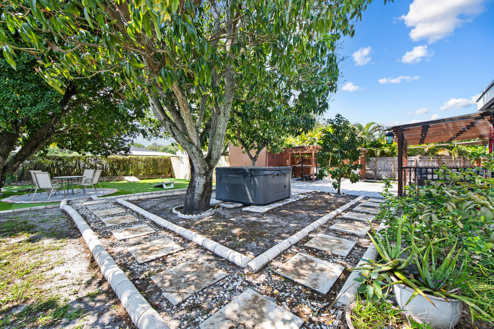 Backyard garden with stone paths, shade trees, and hot tub